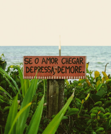 a sign on a wooden post in front of a body of water — Foto por Linoleum Creative Collective na Unsplash