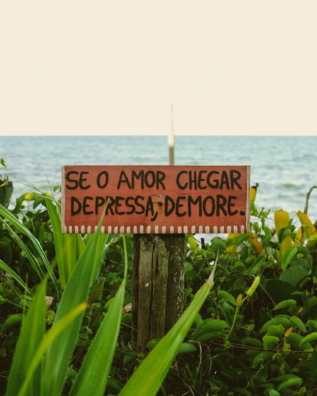 a sign on a wooden post in front of a body of water — Foto por Linoleum Creative Collective na Unsplash