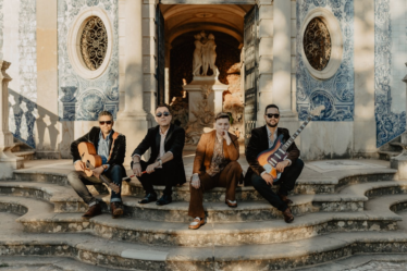 Four musicians posing on stone steps outside building — Foto por Lolla Woodstock na Unsplash