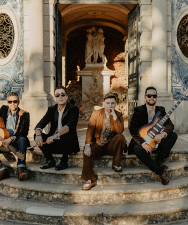 Four musicians posing on stone steps outside building — Foto por Lolla Woodstock na Unsplash