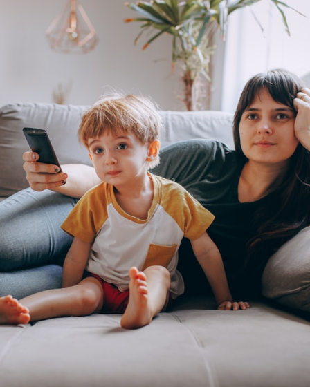 a woman and a child sitting on a couch looking at a cell phone — Foto por Helena Lopes na Unsplash
