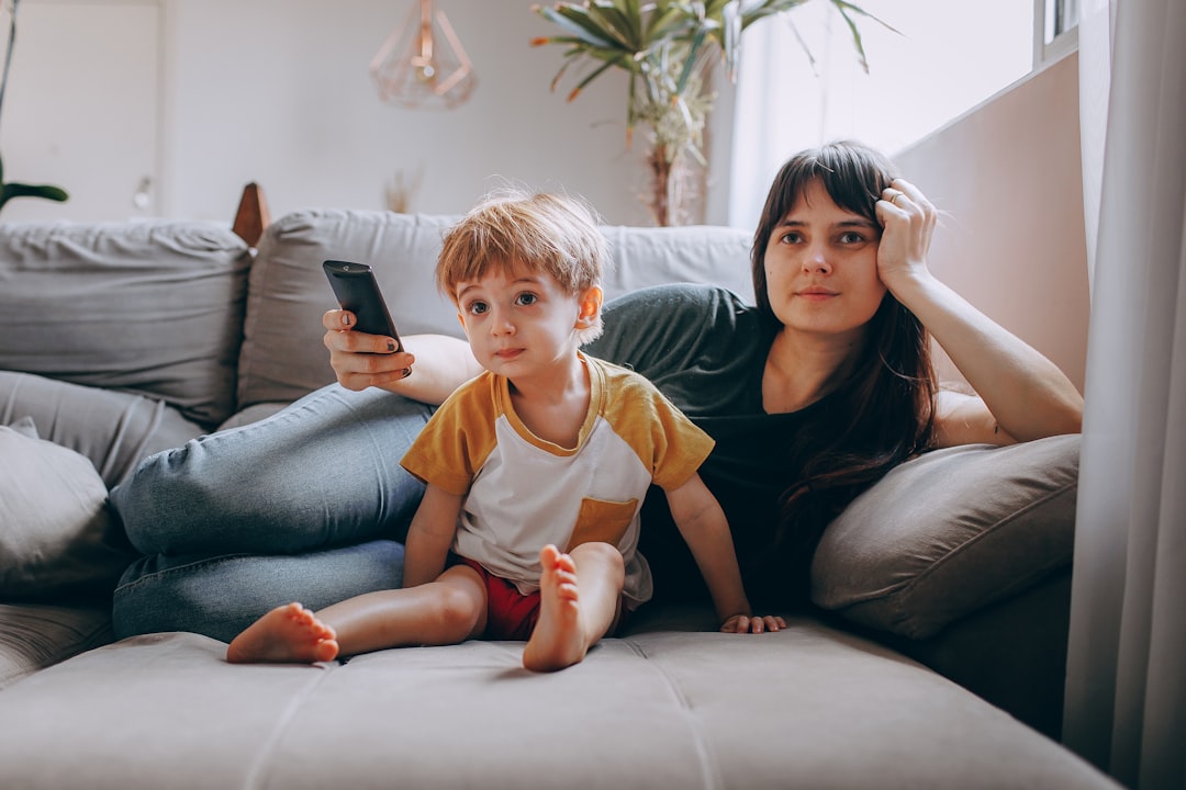 a woman and a child sitting on a couch looking at a cell phone — Foto por Helena Lopes na Unsplash