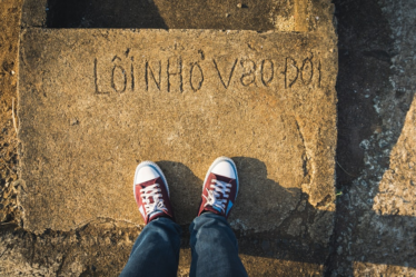 a person standing on a sidewalk with their feet up — Foto por Tien Vu Ngoc na Unsplash