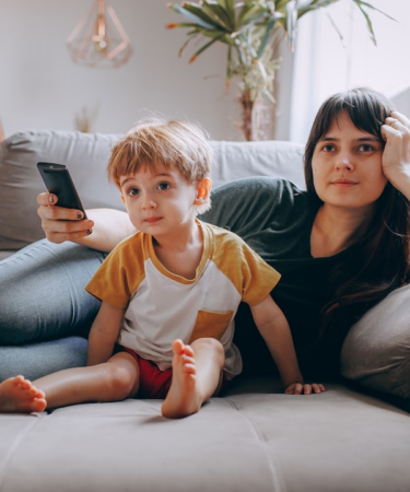 a woman and a child sitting on a couch looking at a cell phone — Foto por Helena Lopes na Unsplash