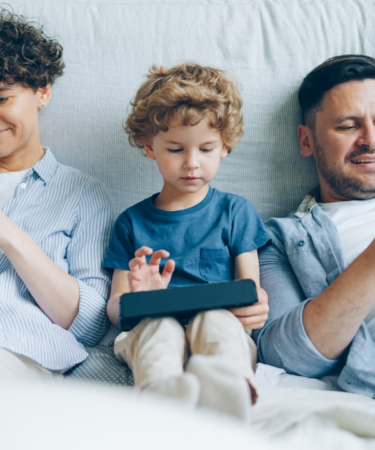 a man, woman and child sitting on a couch looking at their cell phones — Foto por Vitaly Gariev na Unsplash