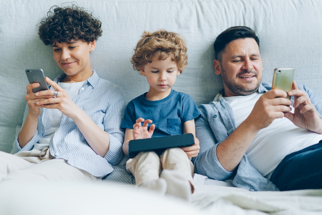 a man, woman and child sitting on a couch looking at their cell phones — Foto por Vitaly Gariev na Unsplash