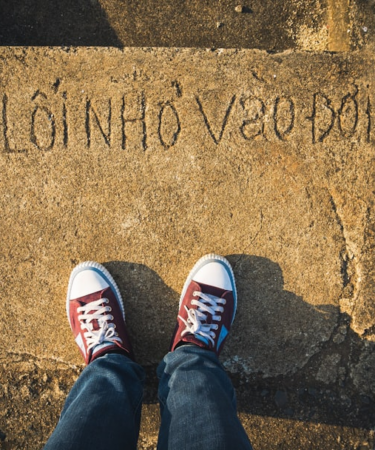 a person standing on a sidewalk with their feet up — Foto por Tien Vu Ngoc na Unsplash