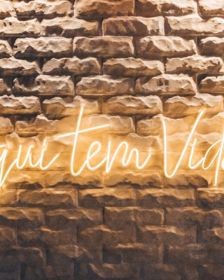 a brick wall with a neon sign on it — Foto por Antonino Visalli na Unsplash